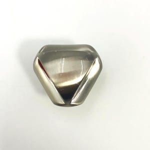May include: A metallic cabinet knob with a triangular shape and rounded corners. The surface has a smooth, polished silver finish with a reflective sheen, featuring a central raised section and a beveled edge design for a modern appearance.