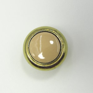 Pode incluir: Um botão redondo dourado com um centro brilhante bege claro. O botão tem um design simples e clássico, adequado para vários projetos de costura ou como elemento decorativo. O diâmetro do botão é de aproximadamente 2,5 cm.