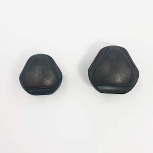May include: Two dark charcoal gray buttons with a rounded triangular shape. Each button features a smooth, matte surface with a subtle, slightly mottled texture and three distinct, recessed linear grooves that form a triangle pattern on the face.