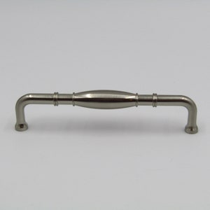 May include: A silver cabinet pull with a curved design. The pull has a slightly rounded, oval-shaped center section.