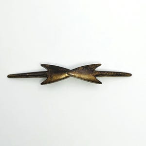 May include: A decorative metal object in a bow-tie design, with a dark brown and gold finish. The piece has pointed, arrow-like ends and an aged, distressed appearance. The object's design suggests it could be an antique or a vintage-style replica.