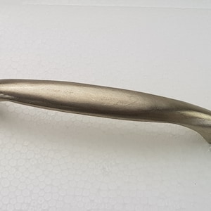 Może przedstawiać: Gałka do szafki z szczotkowanego niklu o zakrzywionym kształcie.