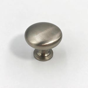 May include: A round cabinet knob with a brushed nickel finish. The hardware features a smooth, domed top surface that transitions into a tapered cylindrical base, providing a clean and functional design for furniture or cabinetry doors and drawers.