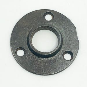 以下が含まれることがあります： 3つの穴とねじ付きの中央開口部を備えた、円形の濃い灰色の金属フランジ。 フランジはわずかに粗く、テクスチャ加工された表面を持ち、鋳鉄または同様の材料で作られているようです。 配管または機械用のコンポーネントです。