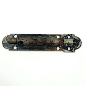 May include: An antique metal bolt latch with a distressed finish. The latch is primarily black with areas of rust and wear, and features a sliding bolt mechanism. The overall design is rectangular with rounded ends and multiple screw holes.