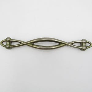 May include: An antique silver-toned drawer pull with a unique, intertwined design. The handle features a central oval opening and decorative end pieces. This hardware piece is ideal for adding a vintage touch to furniture.