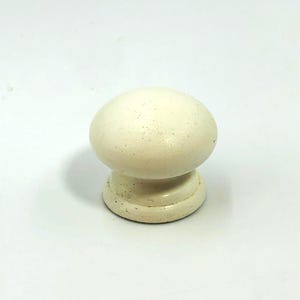 May include: Cream-coloured wooden cabinet knob with a rounded top and a circular base. The knob has a mushroom-like shape and is set against a white background. The knob is likely for furniture.