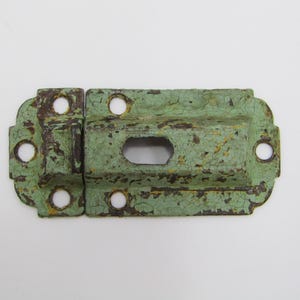 May include: A green metal latch with a keyhole and decorative details. The latch has a distressed, aged look with some rust spots.