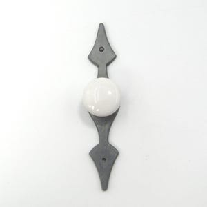 May include: A cabinet pull featuring a grey metal base and a white, spherical knob. The base has a symmetrical design with pointed ends. The hardware is designed for easy installation and adds a touch of elegance to any cabinet or drawer.