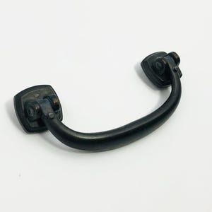 May include: A bronze-toned drawer pull with a curved handle and square mounting plates. The hardware has a vintage aesthetic, suitable for cabinets or furniture restoration projects. The metal has a slightly distressed finish.