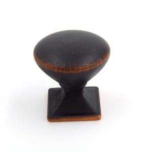 May include: A dark bronze cabinet knob with an oval top and a square base. The knob has a distressed finish with hints of copper-colored accents, suitable for drawers or cabinets.