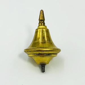 May include: A gold-coloured finial with a decorative design. The finial has a conical top and a bell-shaped body. A threaded post extends from the bottom. It is likely a decorative element for furniture or other items.