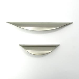 May include: Two brushed nickel cabinet pulls. The top pull is larger than the bottom one. Both have a curved, ergonomic design. The pulls are set against a white background. These are ideal for kitchen or bathroom cabinets.