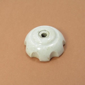 以下が含まれることがあります： 丸みを帯びた上部と基部の周りの湾曲したくぼみを持つ白いセラミックノブ。中央に穴があり、わずかに古びた外観で、ヴィンテージまたはアンティークである可能性があります。