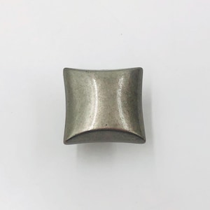 May include: A square cabinet knob with a metallic silver finish and a smooth, slightly concave surface. The knob features rounded corners and a uniform, reflective texture, presenting a clean and simple geometric shape for furniture hardware.