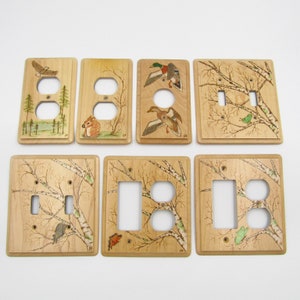Könnte beinhalten: Satz von acht Holz-Lichtschalter- und Steckdosenabdeckungen mit verschiedenen Naturmotiven. Die Motive umfassen ein Eichhörnchen, eine fliegende Ente, einen Weißkopfseeadler und Birken mit Vögeln.