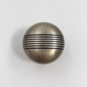 May include: A spherical cabinet knob with a metallic silver finish and a weathered, textured surface. The centre of the knob features a series of five horizontal, recessed black lines that wrap around the circumference of the round object.