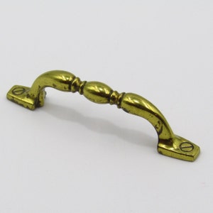 Könnte beinhalten: Ein goldfarbener Metall-Schrankgriff mit gebogenem Design und leicht strukturierter Oberfläche.