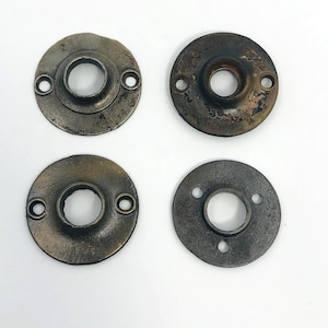 Könnte beinhalten: Vier antike Türknauf-Rosetten in Bronzetönen. Jede Platte ist kreisförmig mit einem zentralen Loch und kleineren Löchern für Schrauben. Das Metall hat ein verwittertes Aussehen, das auf Alter und Gebrauch hindeutet. Diese Platten sind wahrscheinlich für Vintage- oder antike Türbeschläge.