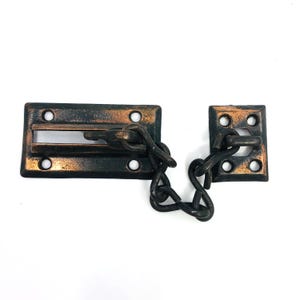 May include: A vintage-style door chain lock with a rectangular plate and a square plate, both with a dark bronze finish. The chain is attached to both plates. The lock is designed to secure a door.