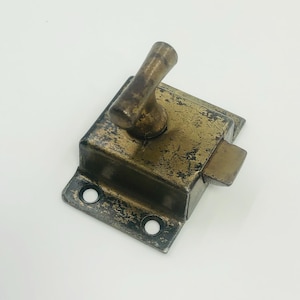 May include: An aged brass-coloured latch with a rectangular body and a curved handle. The latch shows signs of wear and tear, with a distressed finish. Two screw holes are visible on the base. This hardware piece is suitable for vintage furniture or restoration projects.