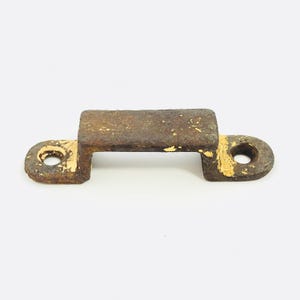 May include: A weathered, rusty metal bracket with a rectangular center and rounded ends, each featuring a hole. The bracket has remnants of yellow paint, suggesting it was once a different color. The object is likely a vintage hardware piece.