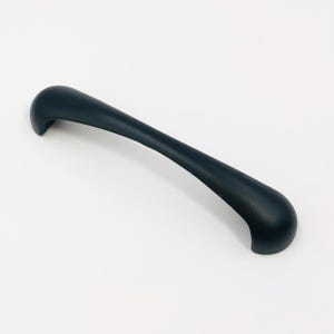 May include: A matte black cabinet handle with a smooth, arched, and elongated design. The hardware features a solid, curved body that tapers slightly toward the ends, providing a clean and functional grip for drawers or cabinet doors.