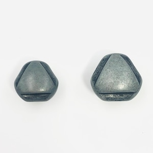 May include: Two dark gray buttons with a smooth, metallic finish. Each button features a rounded triangular shape with a recessed center triangle design. The buttons are presented in two different sizes, both displaying a consistent dark, matte-toned surface texture.
