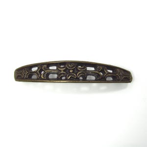 May include: Bronze-colored, curved furniture pull with an openwork design. The decorative hardware features a series of repeating floral and geometric patterns. The pull is likely made of metal and is set against a white background.