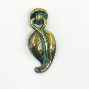 May include: A bronze-toned leaf-shaped drawer pull with a circular top and a loop connecting the two. The leaf has green accents, adding a touch of colour to the metallic finish. This decorative hardware is suitable for cabinets and furniture.