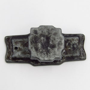 May include: A vintage metal door knocker with a rectangular base and a decorative, octagonal-shaped top. The knocker is silver in colour and has a worn, aged appearance.