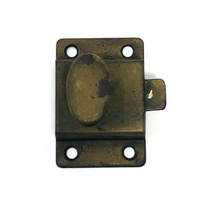 Op de afbeelding: Een vintage messingkleurige grendel met een ovale handgreep en een rechthoekige basis. De grendel heeft vier schroefgaten en een kleine, rechthoekige sluiting. Het metaal vertoont tekenen van ouderdom en slijtage, met een licht aangetaste uitstraling.