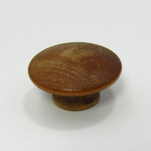 Pode incluir: Puxador de armário redondo de madeira, com acabamento castanho escuro. O puxador tem um topo plano e circular e uma base curta e cilíndrica. O veio da madeira é visível. Adequado para móveis.