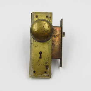 Könnte beinhalten: Antiker Türknauf und Schloss aus Messing mit einem runden Knauf und einem Schlüsselloch. Das Schloss ist an einer rechteckigen Platte befestigt.
