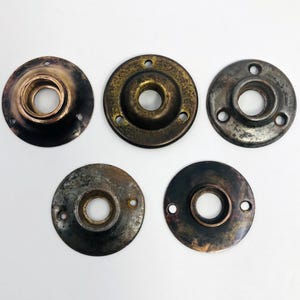 May include: Five antique metal escutcheons with varying patinas. The escutcheons are circular with a central hole and several smaller holes for mounting. The metal finishes range from bronze to dark gray, showing signs of age and wear.