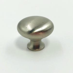 Puede incluir: Un pomo de armario de níquel cepillado con forma ovalada. El pomo tiene una parte superior redondeada y una base corta y cilíndrica. El acabado metálico tiene un aspecto sutil y texturizado. Adecuado para cajones y armarios.