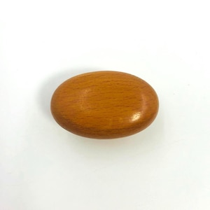 Puede incluir: Un objeto de madera liso, de forma ovalada, con un color marrón claro y cálido. La veta de la madera es visible, añadiendo textura a la superficie. El objeto está sobre un fondo blanco liso.
