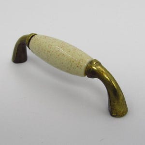 May include: A ceramic cabinet knob with a speckled cream finish and a brass base.