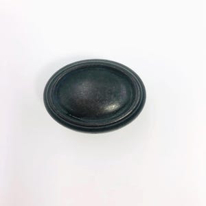 May include: Oval-shaped, antique bronze cabinet pull with a raised, ridged design. The hardware is a dark, muted bronze color and is likely made of metal. This decorative knob is suitable for drawers and cabinets.