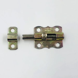 May include: A gold-toned Stanley brand barrel bolt latch set. The set includes the main bolt mechanism and a separate receiver. The bolt has a rounded handle and is designed to be mounted with screws. The text "STANLEY MADE IN USA" is visible.