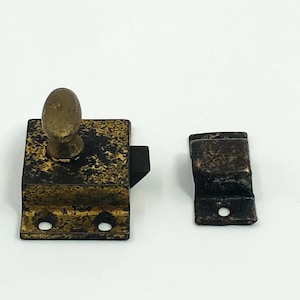 May include: Antique brass-toned cabinet latch set. The set includes a rectangular base with an oval knob and a separate catch. The metal has a distressed, aged appearance with dark spots, suggesting age and use. The latch has two screw holes.