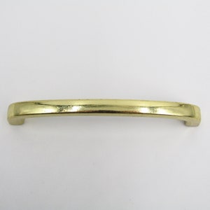 Könnte beinhalten: Ein goldfarbener, gebogener Metallgriff für eine Schranktür.
