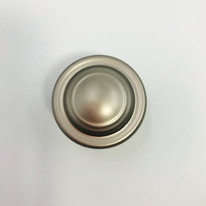 May include: A brushed nickel cabinet knob with a circular design. The knob features a raised center and a surrounding ring, all in a muted silver color. This hardware is suitable for drawers and cabinets.