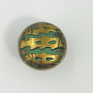May include: A round brass cabinet knob featuring a raised relief design of three fish swimming in a horizontal formation. The background between the fish figures is filled with a matte green enamel finish, contrasting with the metallic gold tone.