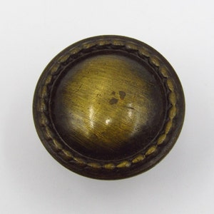 May include: A round, brass cabinet knob with a decorative, rope-like border. The knob has a slightly aged, antique finish.
