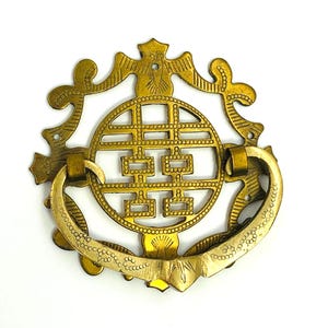 May include: Ornate brass drawer pull with a circular design featuring a double happiness symbol. The pull has a curved handle and decorative flourishes, perfect for adding a touch of vintage charm to furniture.