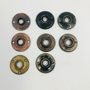 May include: A collection of seven antique door rosettes in various metallic finishes, including bronze, brass, and black. Each rosette features a central hole and multiple screw holes around the perimeter, showcasing aged patina.