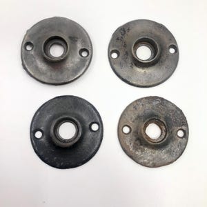 Könnte beinhalten: Vier antike, kreisförmige Türbeschläge aus Metall. Jedes Teil hat ein zentrales Loch und zwei kleinere Löcher zur Befestigung. Das Metall hat ein verwittertes, gealtertes Aussehen mit Farbvariationen von Dunkelgrau bis zu einem helleren, gesprenkelten Finish.