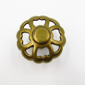 May include: A gold-toned metal cabinet knob with a decorative, openwork design resembling a flower with six petals.