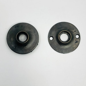 May include: Two antique bronze-colored metal ceiling plate covers. Each plate is round with a central hole and a raised rim. One plate has two screw holes, while the other has none. The plates have a distressed finish.